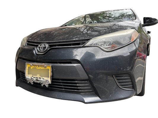 Decorative chrome license plate frame with sculpted bow details installed on a car, standard U.S. fit